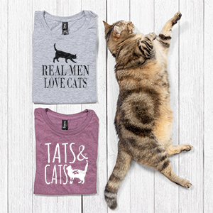 Cute cat lying beside two custom printed t-shirts that read: Real Men Love Cats and Tats and Cats.
