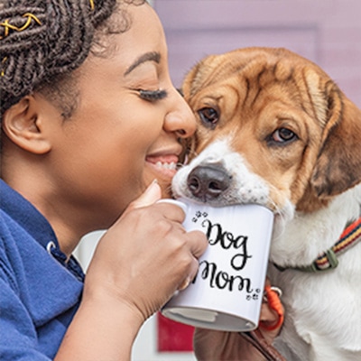 Adorable dog being snuggled by its owner while drinking from a mug that reads: Dog Mom.