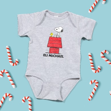 Baby bodysuit in a Christmas setting with a custom designed official licensed personalized PEANUTS® design showing Snoopy and Woodstock sitting atop the doghouse.