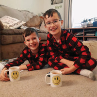 Twin boys wearing matching PJs sitting on the floor drinking from their matching coffe mugs with smiley faces.