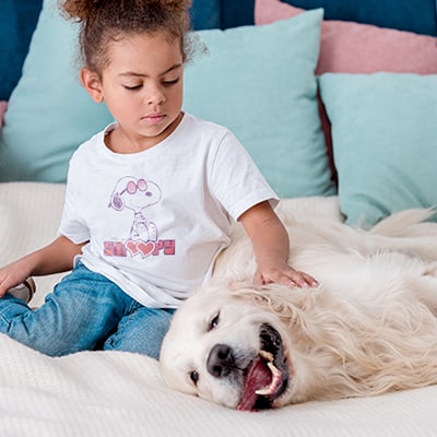 Little girl with her dog. The girl is wearing a t-shirt with an official licensed PEANUTS® Snoopy love design.
