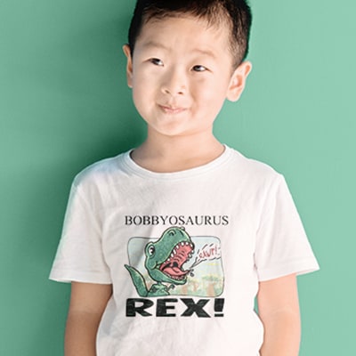 Young Asian American boy wearing a custom printed t-shirt with personalizable area and dinosaur illustration. Personalized text reads: Bobbyosaurus Rex.