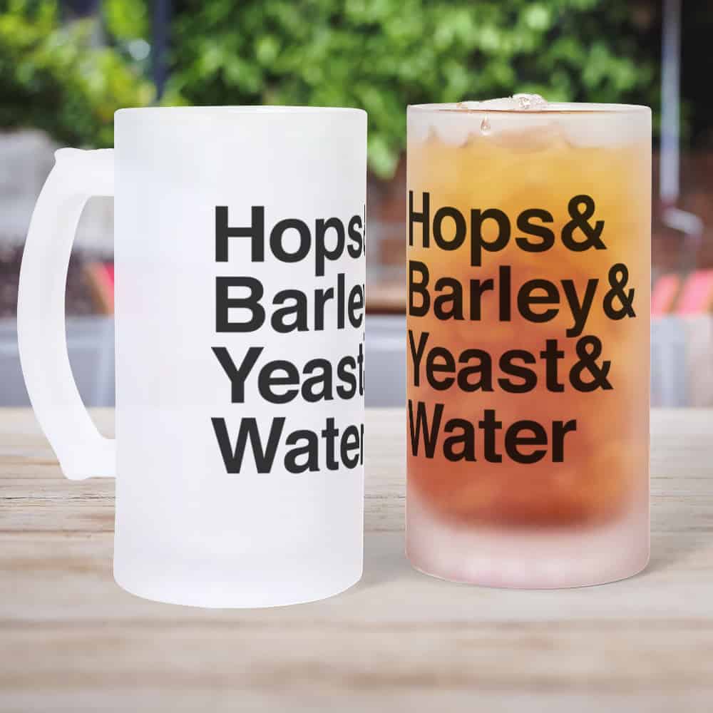 Two frosted beer steins sitting on a table. One is empty and the other full. Each have the same design which reads Hops and Barley and Yeast and Water.