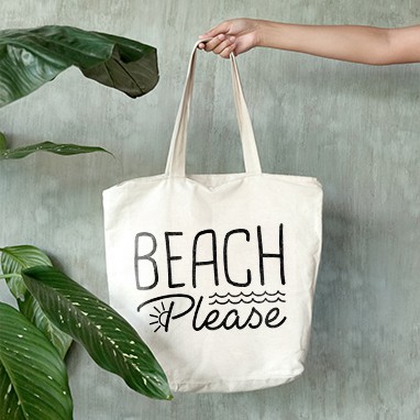 A tote bag being held with a text design that reads Beach Please.