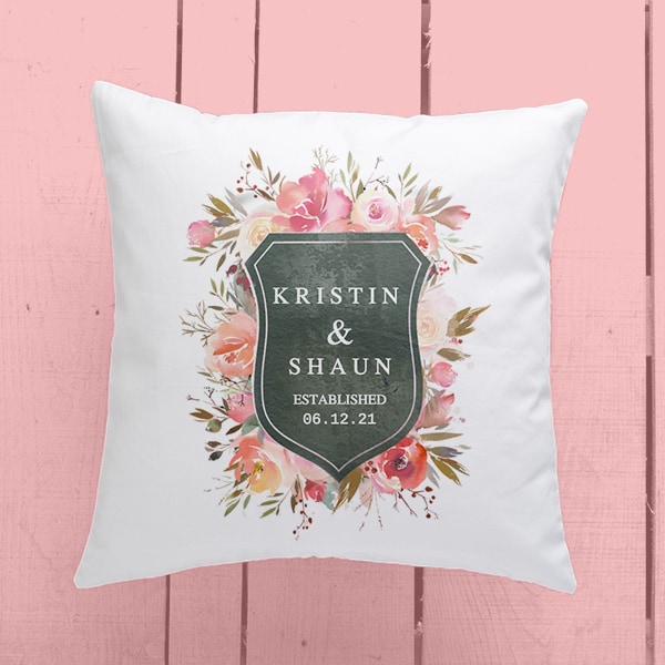 A personalized pillow with a design reading - Kristin & Shaun with their wedding date, laying on a wooden table that has been stained pink.