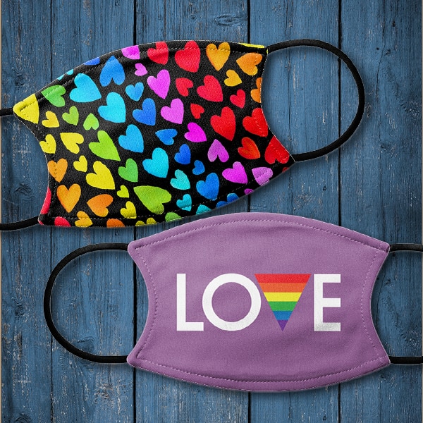 Two custom printed face masks against a blue wooden table. The top mask has a heart design pattern where different sections of the pattern are the colors of the rainbow. The second mask is purple and has a text design reading Love. The V is the upside down triangle with the rainbow pattern.