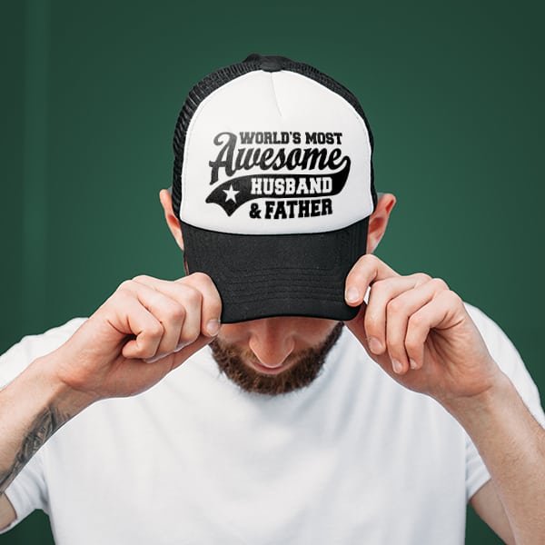 A husband showing off his hat with a custom design that says World's Most Awesome Husband and Father.