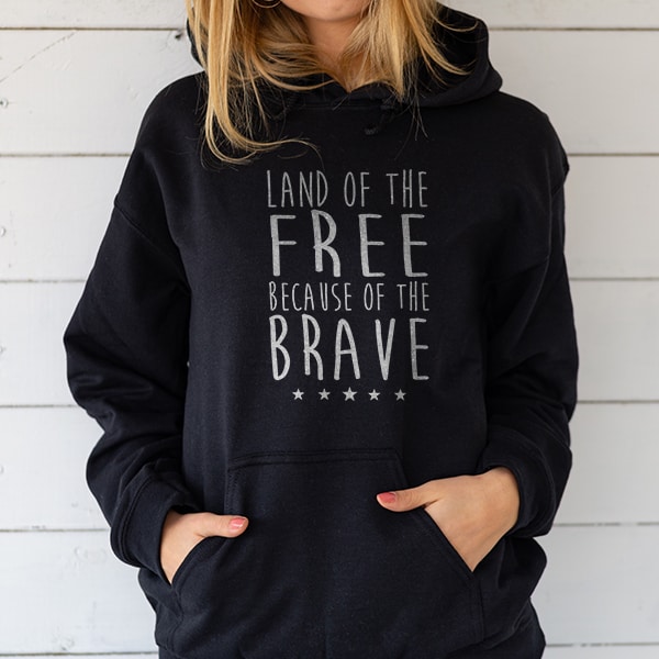 Woman in a Navy blue hoodie with a custom stylized text design that reads: Land of the Free Because of the Brave