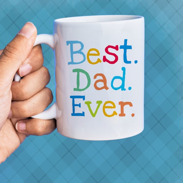 A closeup shot of a mug with a Best Dad Ever design on it with the letters in multiple varying colors.