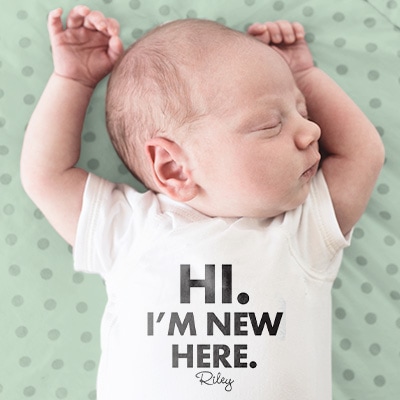 Adorable baby wearing baby bodysuit with custom stylized text design reading: Hi. I'm New Here. and a place to personalize the baby name.