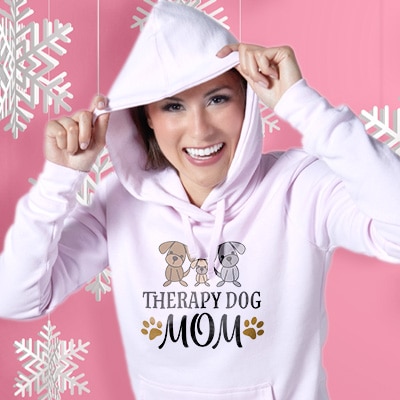 Woman in pink hoodie with custom design with cure puppy illustrations and stylized text that reads: Therapy Dog Mom.
