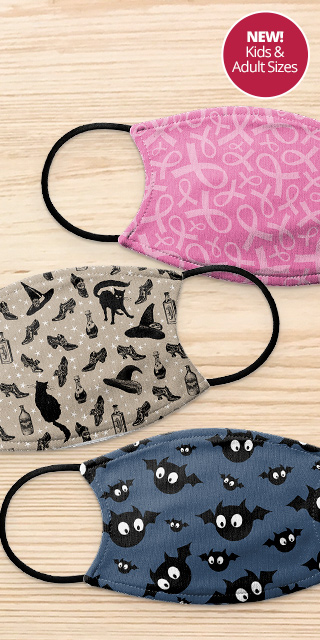 3 Custom designed face masks on a wooden table. One has a pink breast cancer awareness ribbon print pattern, one is a halloween print with witch hats and potion bottles, and one is a navy mask with a cartoon bat print.