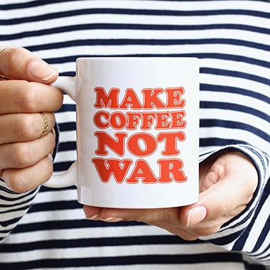 A woman holding a mug in front of her with a design that reads Make Coffee Not War.