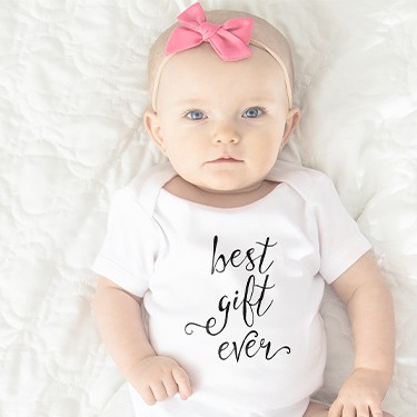 Baby lying on bed in white baby onesie with text design that reads: best gift ever.